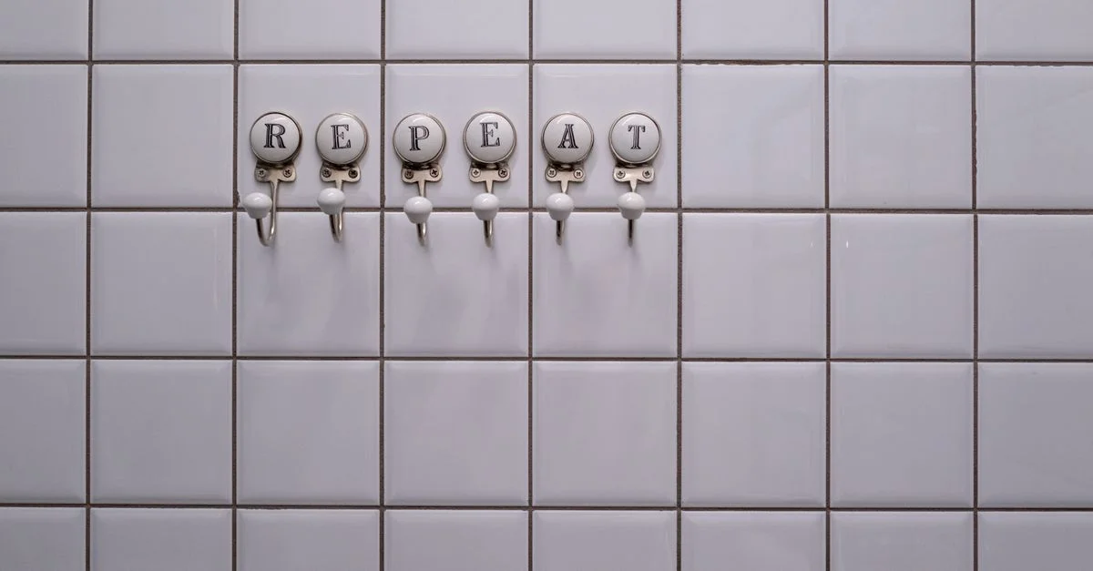 Mur en carrelage blanc avec des crochets à serviette épelant 'RÉPÉTER', mettant en valeur un design minimaliste conceptuel.